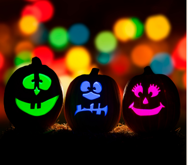 Three pumpkins carved with faces in green, blue and pink colors