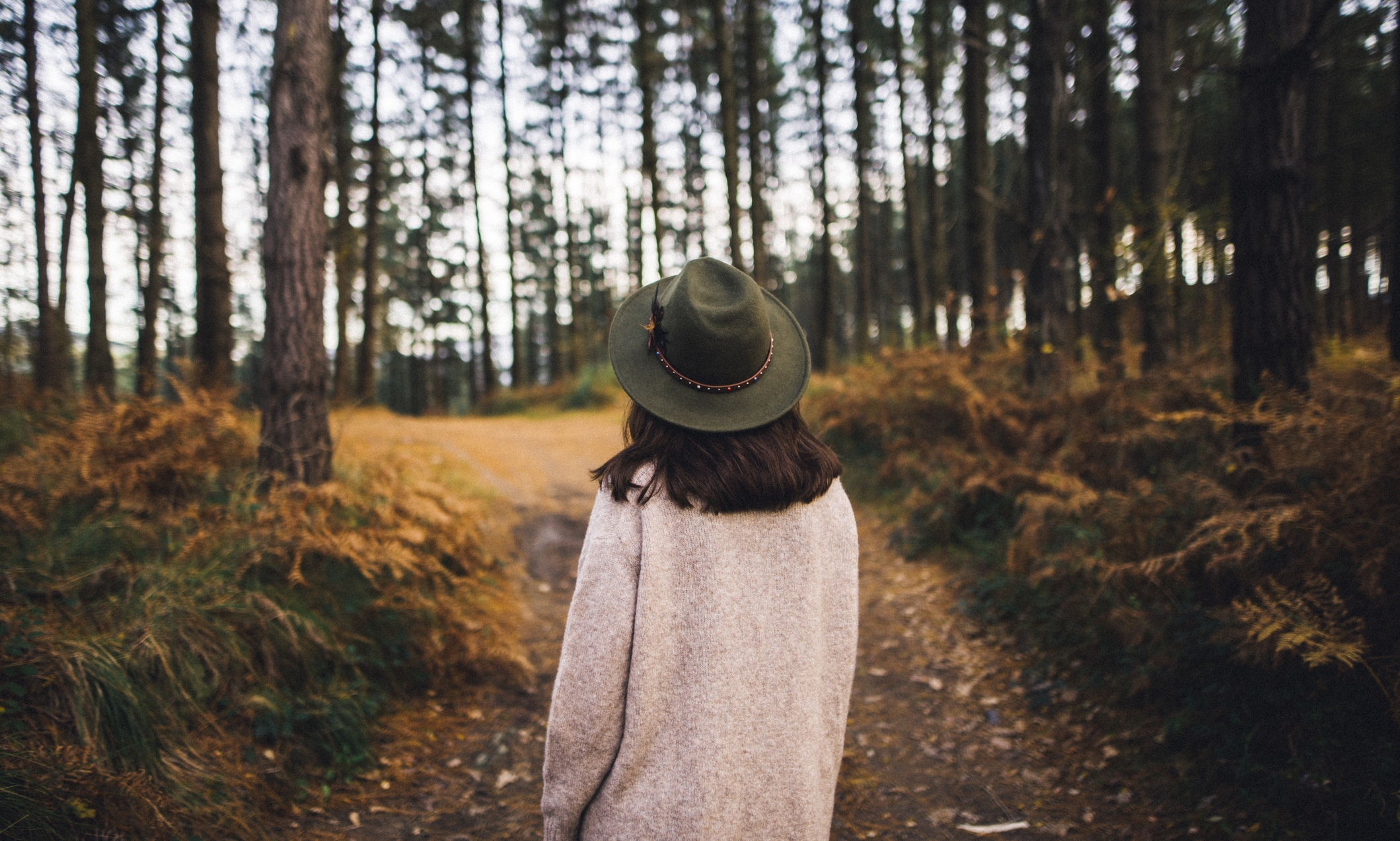 A young woman wearing a hat and walking by a beautiful forest area